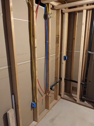 Professional plumbing installation of PEX water lines and drainage pipes within the wall framing of a residential home